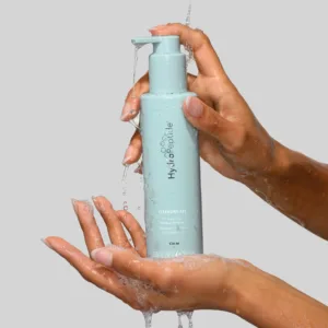 Hands pumping a light blue cleansing gel bottle, with gel and water droplets on the bottle and hands