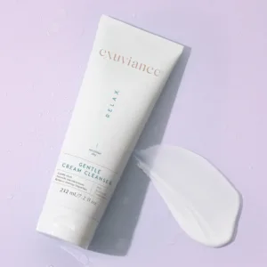 Exuviance Relax Gentle Cream Cleanser tube on a light purple surface with a dollop of cream beside it.