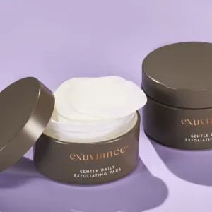 Open jar of Exuviance Gentle Daily Exfoliating Pads with two white pads on a lavender background.