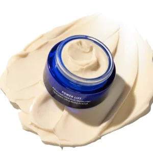 Blue glass jar of moisturizer with thick beige cream smeared around it, on a pale surface.
