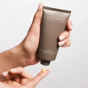 Hand squeezing a brown tube labeled 'exuviance Advanced Series' to dispense a small amount of cream onto a fingertip; close-up product shot.