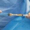 Close-up of hands in blue gloves preparing a syringe on a blue sterile drape.