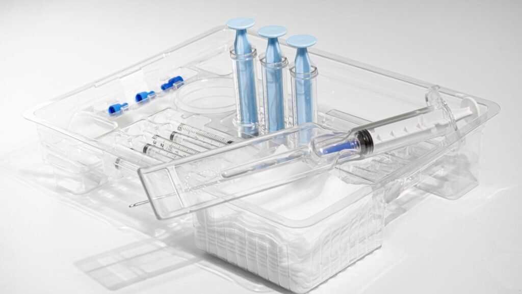 Transparent medical kit holding syringes and blue-capped vials, arranged in a clear plastic tray.
