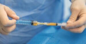 Close-up of hands in blue gloves preparing a syringe on a blue sterile drape.