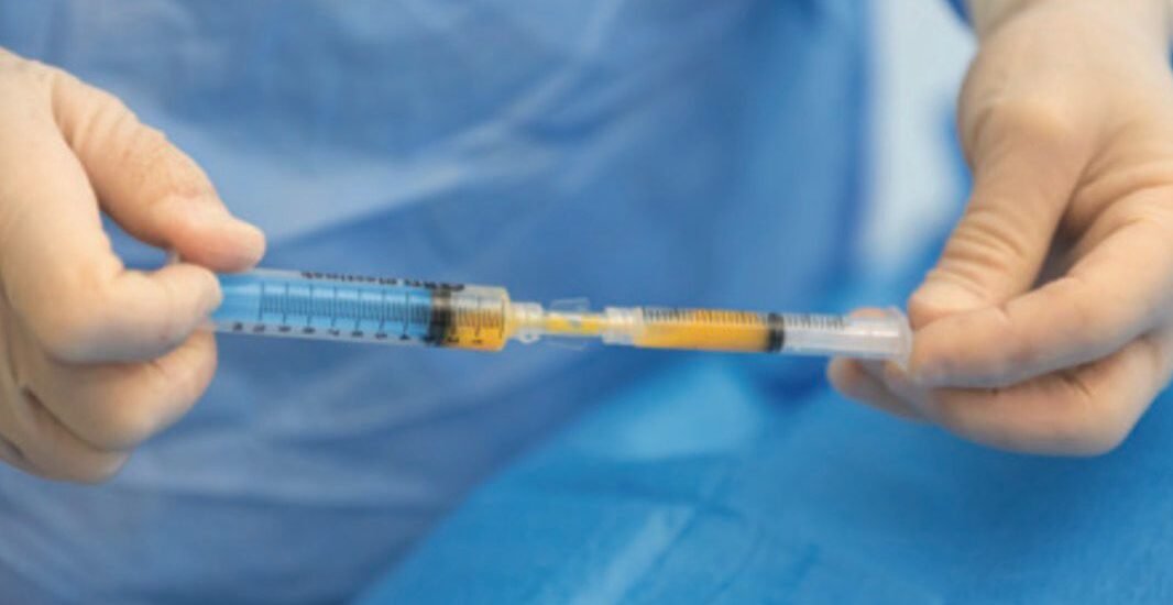 Close-up of hands in blue gloves preparing a syringe on a blue sterile drape.