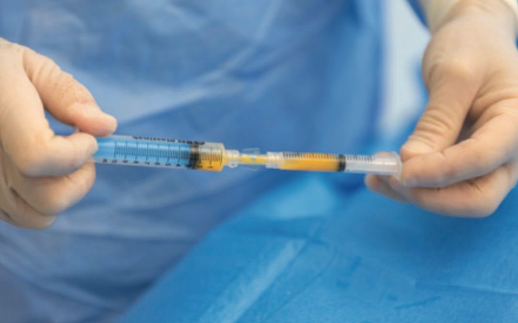 Close-up of hands in blue gloves preparing a syringe on a blue sterile drape.