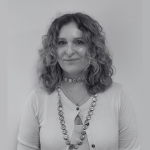 Bust‑length, grayscale portrait of a smiling woman with shoulder‑length curly hair, wearing beaded necklaces and a light cardigan.